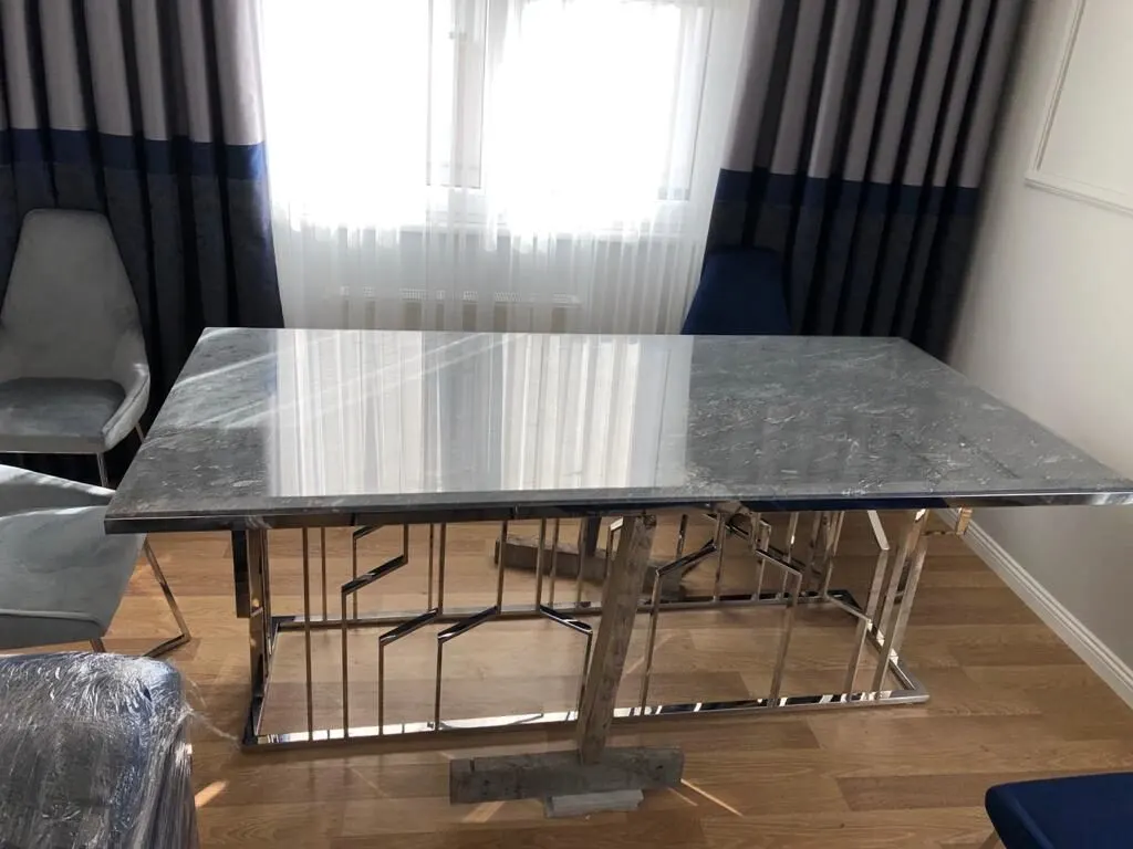 Yemek odasında, mermer tablalı ve krom kaplamalı geometrik gövdeli yemek masası