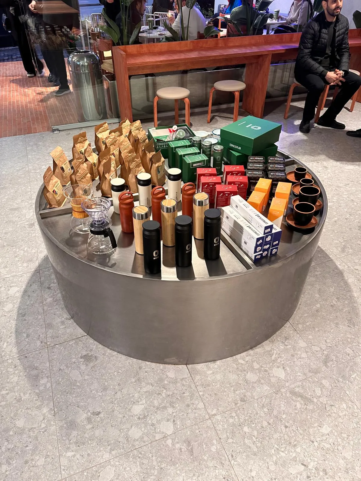 Ürün paketlerinin sergilendiği yuvarlak, kenarlıklı metal teşhir ünitesi