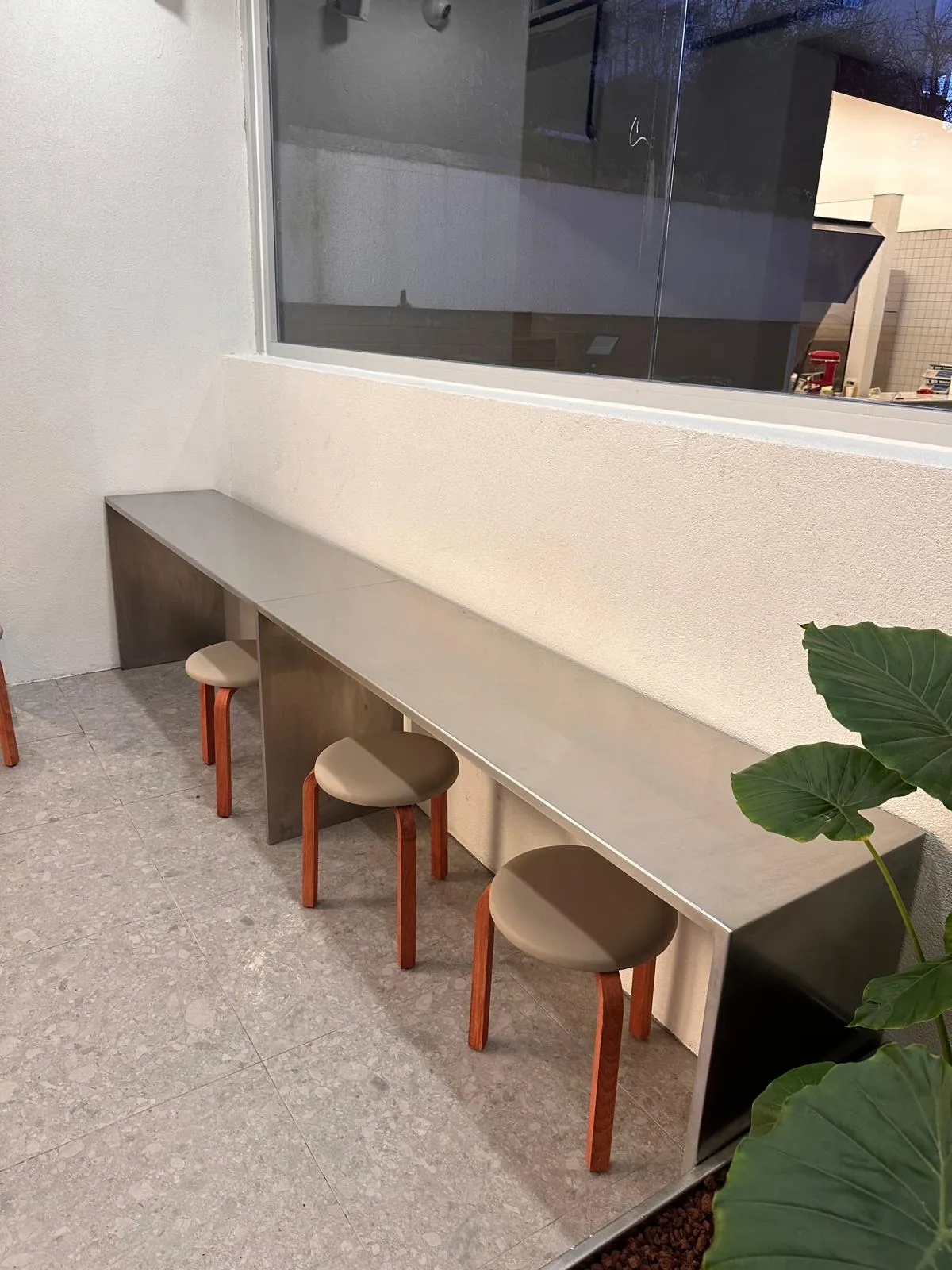 Pencere boyunca uzanan metal tezgâh ve ahşap tabureler